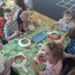 Grupa dzieci siedzi przy stoliku, trzyma w ręce pędzelek i maluje okrągłe papierowe talerzyki.
