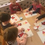 Dzieci siedzące przy stoliku i wykonujące prace plastyczne przedstawiające Mikołaje.