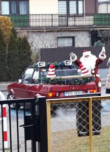 Mikołaj stojący obok samochodu. przed budynkiem przedszkola.