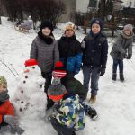 Grupa dzieci stoi na dworze z ulepionym bałwnem. Na dworze jest dużo śniegi.