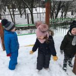 Troje dzieci bawiących się na pokrytym śniegiem przedszkolnym placu zabaw.