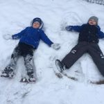 Dwoje dzieci leżących na śniegu w ogrodzie przedszkolnym.
