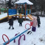 Dzieci bawiące się na pokrytym śniegiem przedszkolnym placu zabaw.