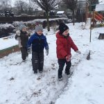 Troje dzieci bawiących się na śniegu na przedszkolnym placu zabaw.