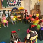 Grupa dzieci siedzących w sali przedszkolnej, w kole na krzesłach. Każde dziecko ubrane jest w strój karnawałowy i trzyma w rękach balona.