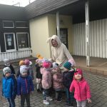 Grupa dzieci stojąca w ogrodzie przedszkolnym wraz z Panią ubraną w strój zajączka wielkanocnego.