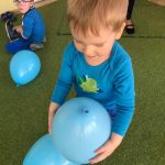 Chłopiec trzyma w rękach balon. Za nim na dywanie siedzi 2 chłopiec.