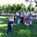 Grupa dzieci znajdująca się w ogrodzie przedszkolnym i uczestnicząca w zabawach sportowych z trenerem.