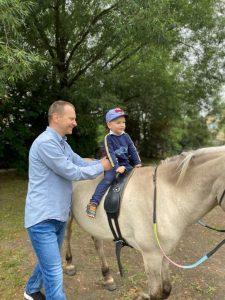 Chłopiec siedzi na koniu. Obok trzyma go tata.