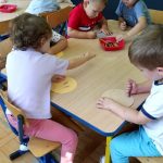 Dzieci siedzą przy stoliku i koloroują papierowe kropki.