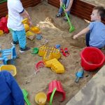 3 dzieci bawi się w piaskownicy.