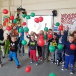 duża grupa dzieci stoi na dywanie w przedszkolnej sali . Dzieci podrzucają kolorowe balony.