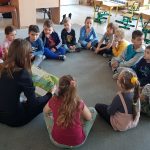 Grupa dzieci i Pani siedzą na dywanie w przedszkolnej sali i słuchają czytanego opowiadania.
