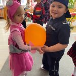 Chłopiec i dziewczynka tańcą z balonem, który trzymają brzuchami.