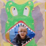 Chłopiec siedzi na plakatem przedstawiającym dinozaura z otwartą buzią.