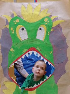 Chłopiec siedzi na plakatem przedstawiającym dinozaura z otwartą buzią.