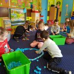 Dzieci na dywanie układają krople deszczu z niebieskich nakrętek.