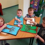 4 dzieci stoi przy stoliku i maluje za pomocą złączonych patyczków.