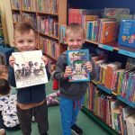 2 Chłopców w bibliotece trzyma książkę w ręce.