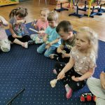 Dzieci siedza na dywanie i grają na instrumentach.