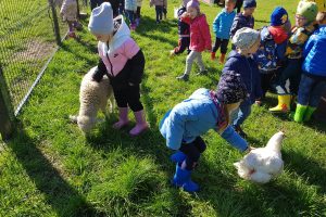 Dzieci, kura oraz owieczka bawiące się na polanie