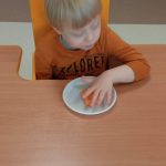Dziecko siedzi przy stoliku. Dotyka masy sensorycznej leżącej na stole na talerzyku.