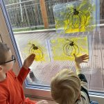 Chłopcy tworzą obrazek dyni z masy sensorycznej w zawieszonych na oknie woreczkach