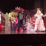 Na brązowej scenie występują postaci: kota, króla, królewny i młynarczyka. Ubrani są w kolorowe stroje. Za nimi scenografia zamku.