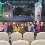 20 dzieci ubranych w kurtki i czapki stoją oparci o scenę teatralną, na której jest scenografia do bajki o Kocie w butach.