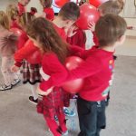 Chłopiec i dziewczynka ubrani na czerwono stoją plecami do siebie i pomiędzy trzymają czerwony balon. Tańczą do muzyki.
