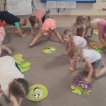 Dzieci ćwiczą gimnastykę z użyciem dużych warzyw i owoców tekturowych.