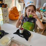 Dziewczynka próbuje zielony koktajl. Na stole leży talerzyk w kształcie kotka i smaczny deser.