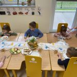 Siedmioro dzieci siedzą przy stolikach przy wielkanocnym śniadaniu.