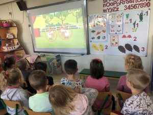 Dziewięcioro dzieci siedzących na krzesłach i oglądających bajkę na tablicy interaktywnej