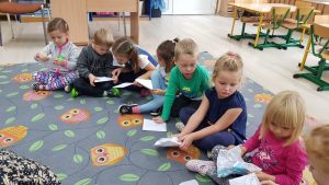 Ośmioro dzieci siedzących na dywanie i trzymających kartki papieru