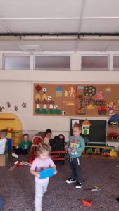 Pięcioro dzieci bawiących się na dywanie. Obok nich chłopiec siedzący na krześle.
