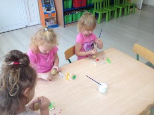 Trzy dziewczynki siedzące przy stoliku i ozdabiające ziemniaki.