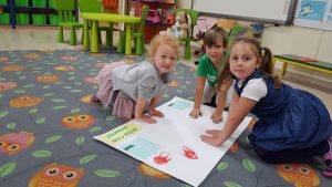 Troje dzieci odbijających pomalowane farbami dłonie na brystolu