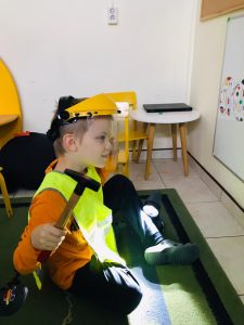 Chłopiec siedzący na dywanie i trzymający w ręku młotek