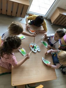 Pięcioro dzieci siedzących przy stoliku i malujących farbami.