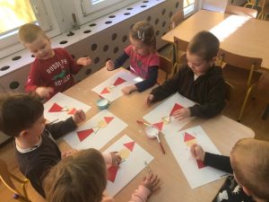 Dzieci siedzące przy stoliku i wykonujące prace plastyczne przedstawiające Mikołaje.