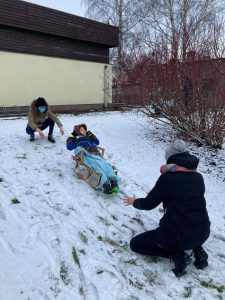 Chłopiec na sankach zjeżdża z górki. na górze i na dole kucają nauczycielki.