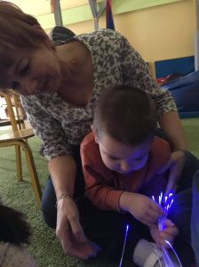 chłopiec siedzi na dywanie i bawi się światłowodami w kolorze niebieskim.