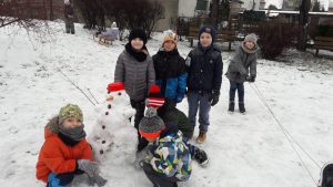 Grupa dzieci stoi na dworze z ulepionym bałwnem. Na dworze jest dużo śniegi.