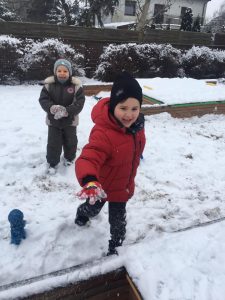 Dwoje dzieci biegnących za sobą na pokrytym śniegiem, przedszkolnym placu zabaw..