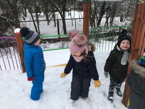 Troje dzieci bawiących się na pokrytym śniegiem przedszkolnym placu zabaw.