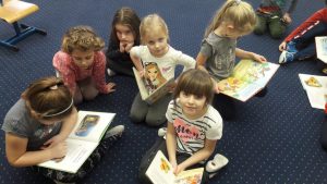 6 dziewczynek siedzi na dywanie. W rękach trzymają otwarte książki.