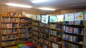 Regały w ksiązkami w bibliotece. Prześ środek zawieszony sznurek z pracami plastycznymi dzieci ( narysowany Kubuś Puchatek)