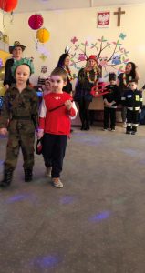 Dwoje dzieci pozujących do zdjęcia w karnawałowych strojach. Z tyłu, za nimi znajdują się cztery panie wraz z dwoma chłopcami, ubranymi w karnawałowych strojach.