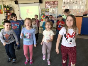 Grupa dzieci gimnastykująca się na dywanie, w sali przedszkolnej.